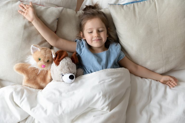Little girl sleeping in bed with fluffy animal toys